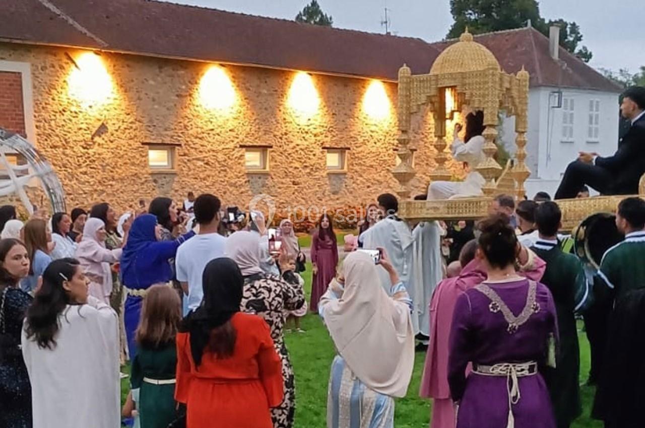 Un groupe de personnes en tenue traditionnelle entoure une scène festive avec une structure décorative dorée.