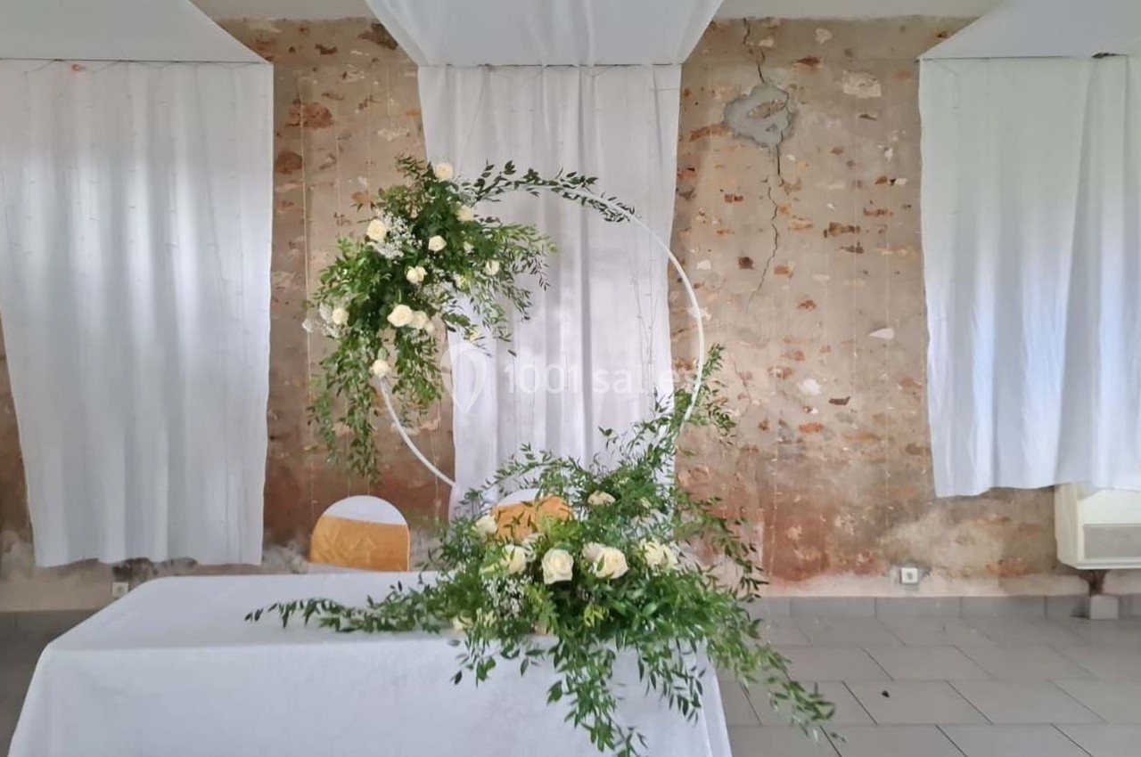 Décoration florale avec roses blanches et feuillage sur une arche circulaire, devant une table drapée de blanc.