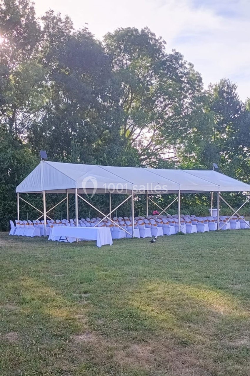 Tente blanche installée sur une pelouse, abritant des tables et chaises alignées pour un événement en plein air.