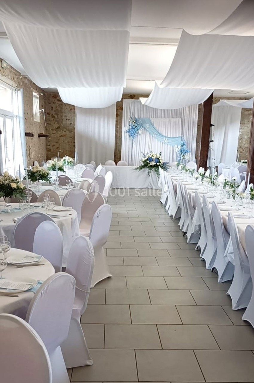 Salle de réception décorée avec des nappes blanches, des chaises houssées et des arrangements floraux bleus et blancs.