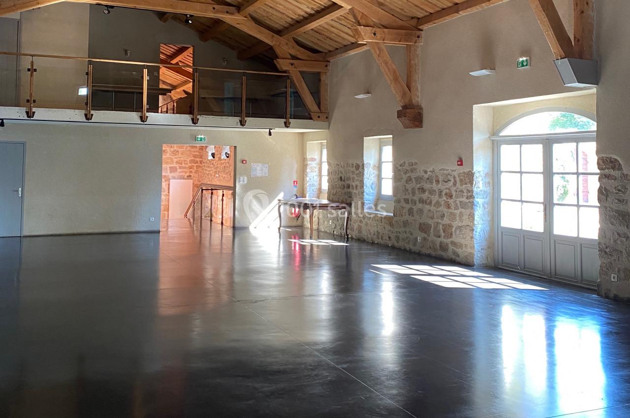 Salle lumineuse avec sol en béton poli, murs en pierre, poutres apparentes et mezzanine en bois.