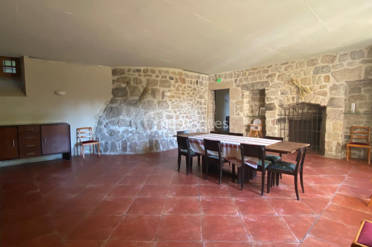 Salle avec murs en pierre, sol en carrelage rouge, table en bois entourée de chaises et meuble en bois contre le mur.