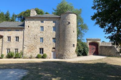 Miniature Location salle Montregard (Haute-Loire) - Château de Marcoux #8 Cour extérieure avec table et chaises en métal, entourée de murs en pierre, d'un bâtiment en pierre et d'arbres.