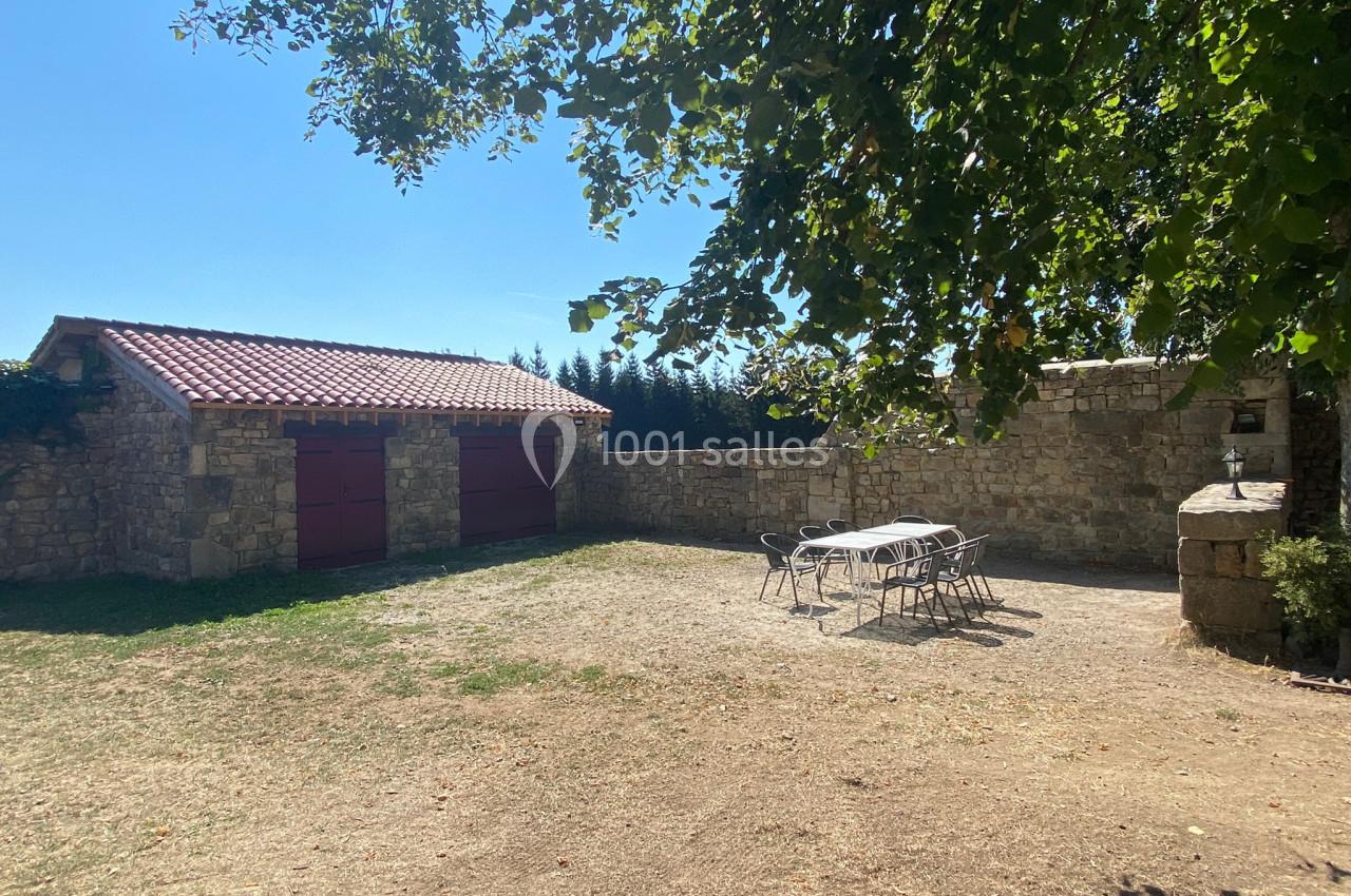 Cour extérieure avec table et chaises en métal, entourée de murs en pierre, d'un bâtiment en pierre et d'arbres.