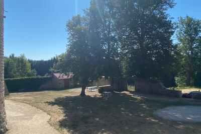 Miniature Location salle Montregard (Haute-Loire) - Château de Marcoux #9 Cour extérieure avec table et chaises en métal, entourée de murs en pierre, d'un bâtiment en pierre et d'arbres.