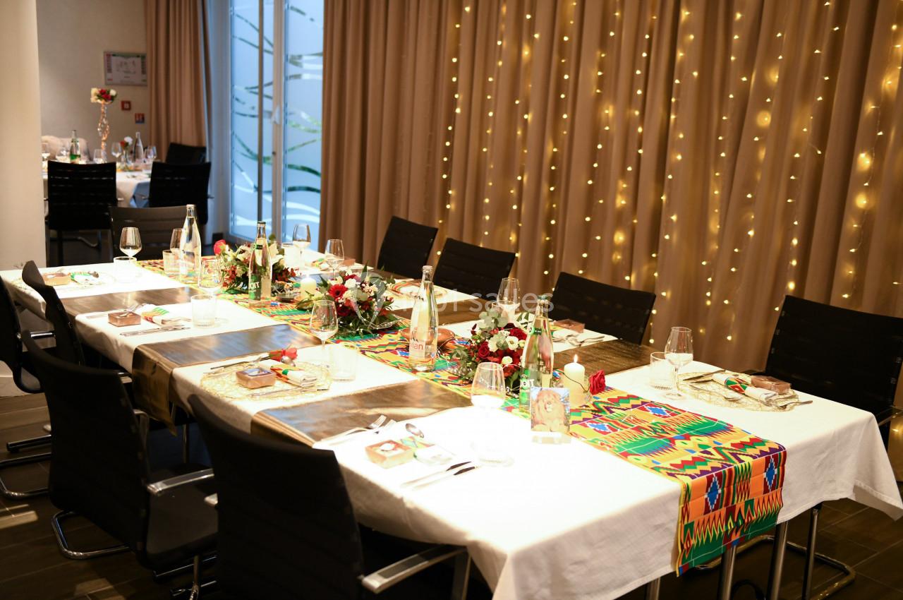 Tables décorées pour un repas festif avec nappes blanches, chemins de table colorés, fleurs et guirlandes lumineuses en…