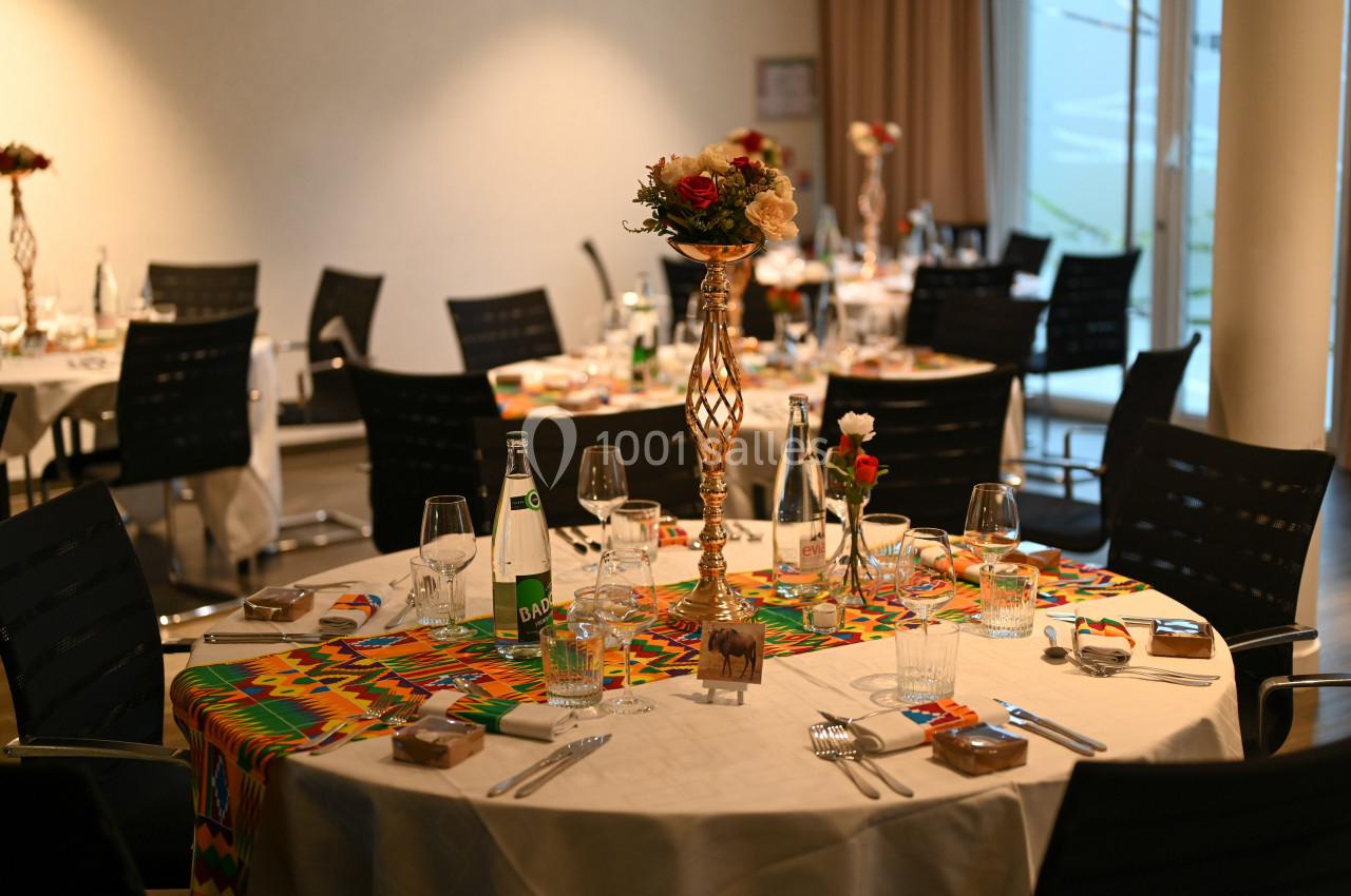 Salle de réception avec tables rondes dressées, décorées de nappes colorées et centres de table floraux.