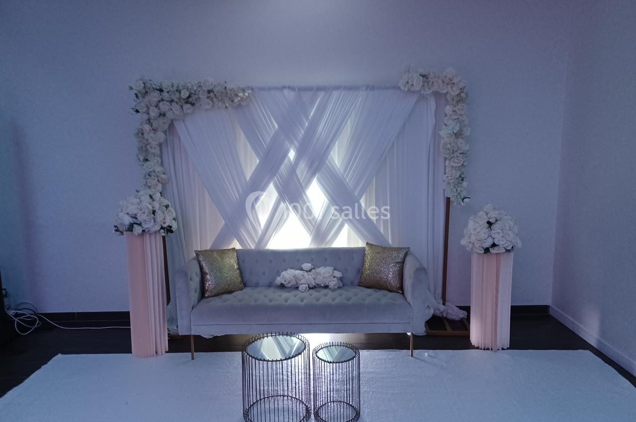 Canapé gris devant un rideau blanc décoré de fleurs blanches, avec deux tables basses et colonnes florales assorties.