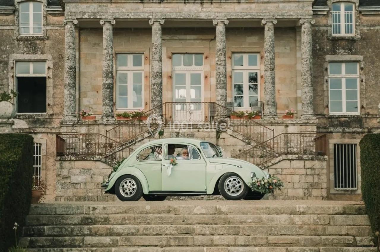 Voiture ancienne verte décorée de fleurs garée devant un bâtiment en pierre avec colonnes et escaliers.