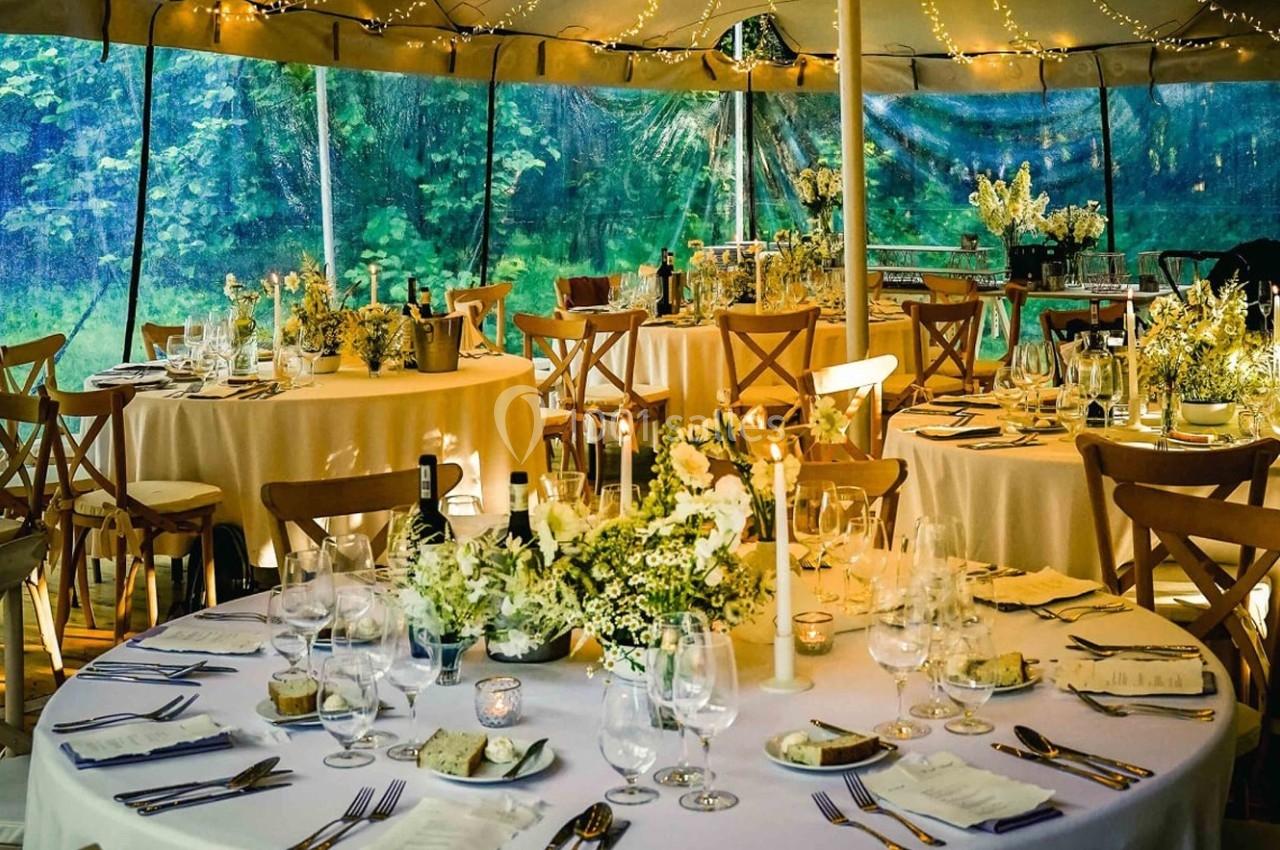 Salle décorée pour un événement avec des tables rondes dressées, des fleurs blanches et un éclairage chaleureux.