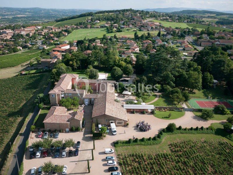 Vue aérienne d'un domaine avec bâtiments en pierre, vignobles, terrains de sport et village environnant.