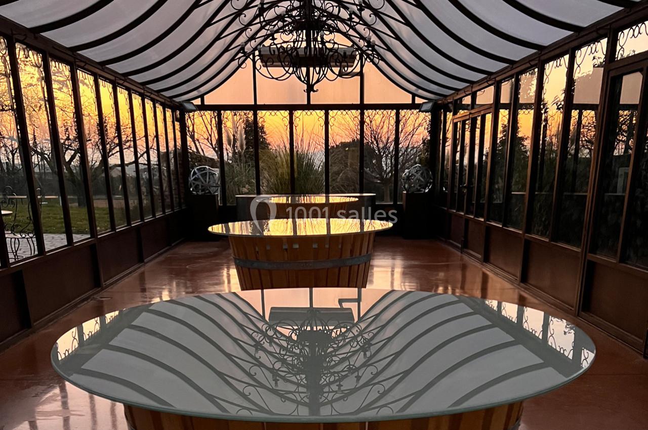 Salle vitrée avec des tables en verre, éclairée par un coucher de soleil visible à travers les grandes baies vitrées.