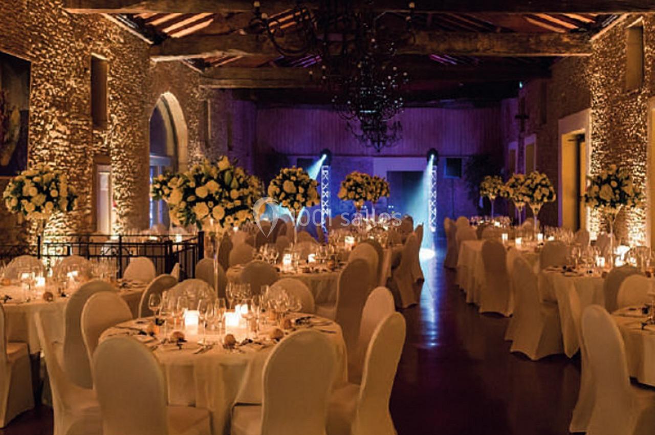 Salle de réception élégante avec tables rondes dressées, chaises blanches et éclairage chaleureux.