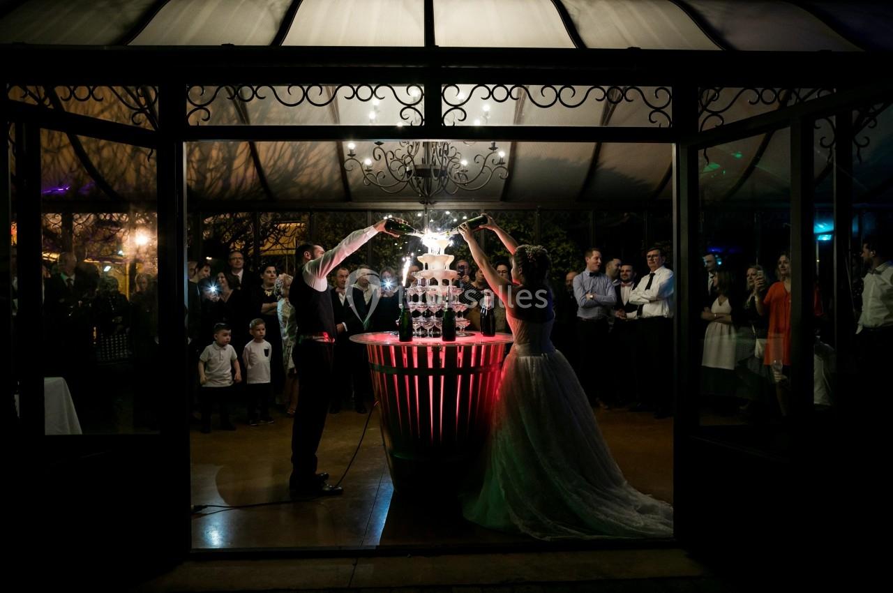 Un couple verse du champagne dans une pyramide de verres lors d'une réception, entouré d'invités.