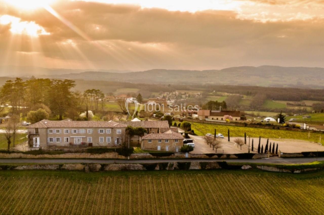 Vue aérienne d'un domaine rural avec bâtiments en pierre, entouré de champs et baigné par une lumière dorée au coucher du…