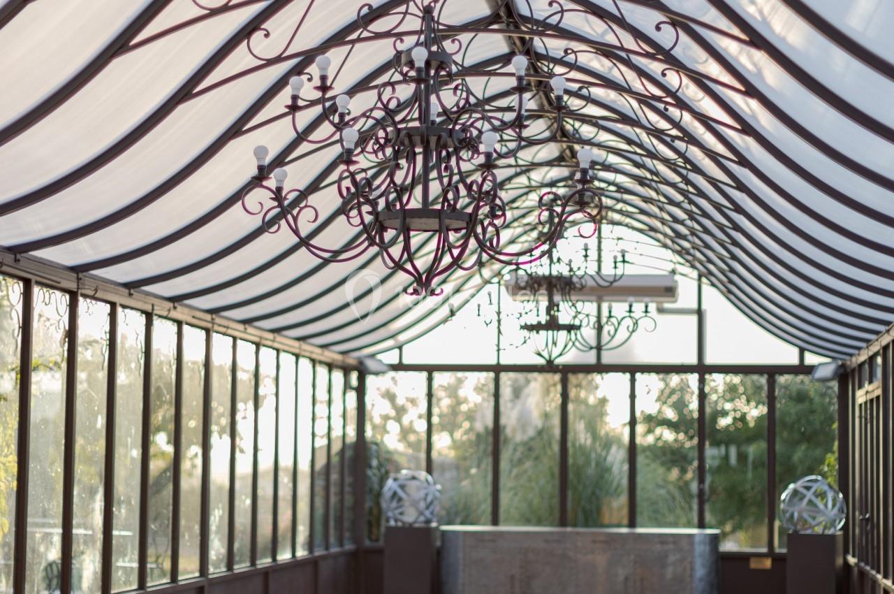 Intérieur d'une serre lumineuse avec un toit en verre, des lustres suspendus et un sol réfléchissant.
