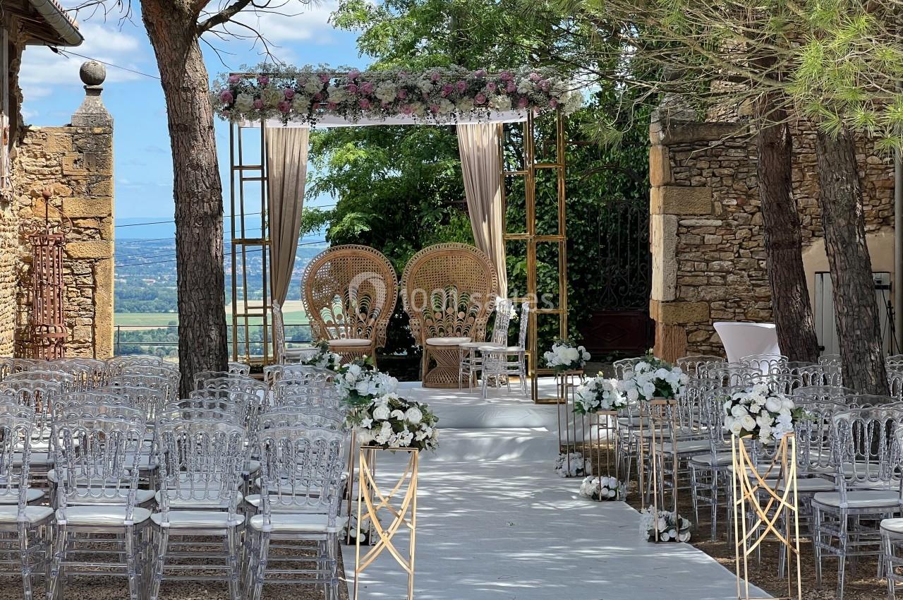 Allée décorée de fleurs menant à une arche ornée de voilages et de fleurs, entourée de chaises transparentes.