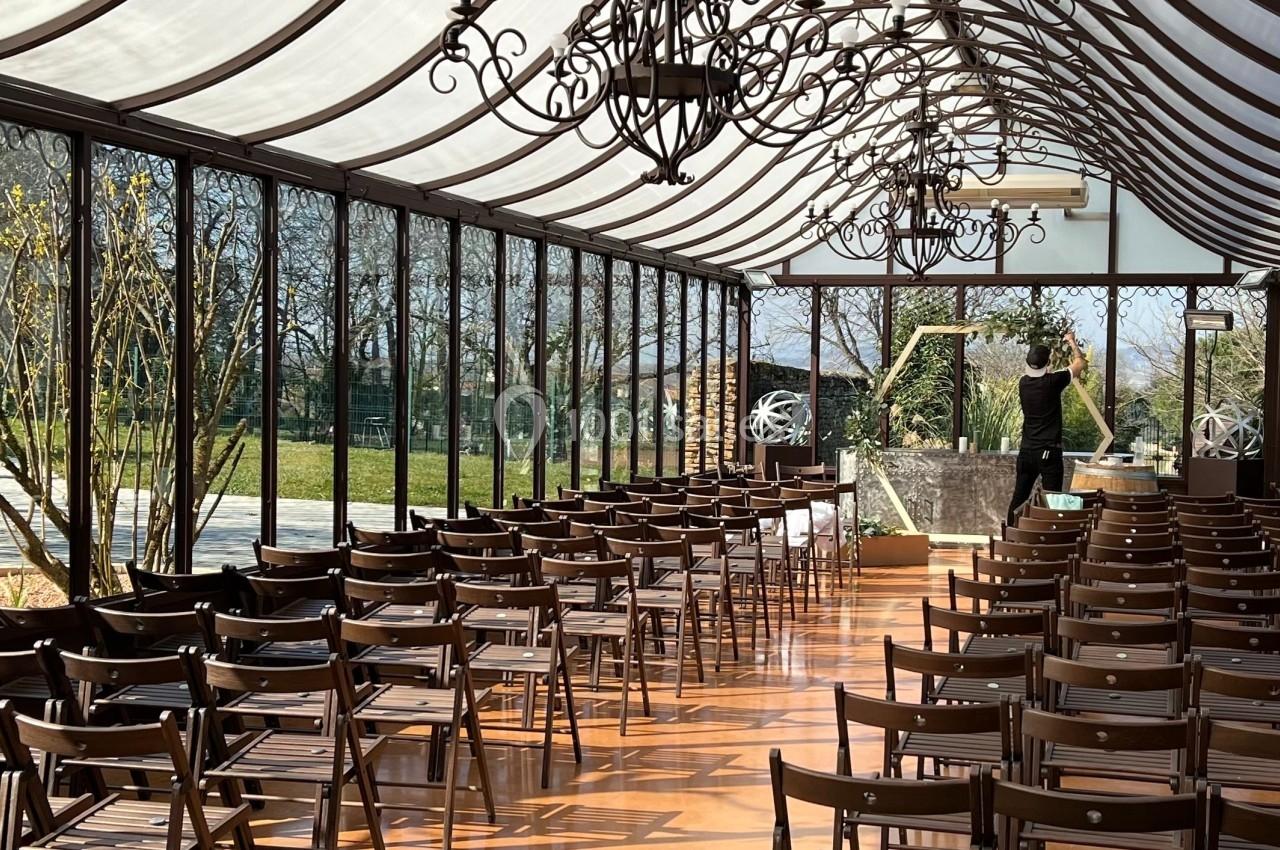 Salle lumineuse avec chaises alignées sous une verrière, décorée de lustres en fer forgé et fleurs.