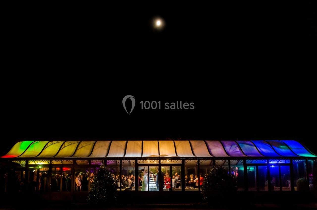 Vue nocturne d'une salle vitrée éclairée par des lumières colorées, avec des personnes visibles à l'intérieur.