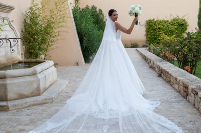 Un couple en tenue de mariage s'enlace dans un champ entouré d'oliviers sous une lumière douce.