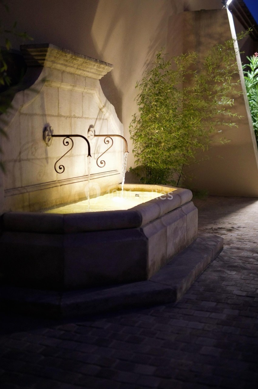 Fontaine murale en pierre avec deux jets d'eau éclairés, entourée de bambous et située sur un sol pavé.