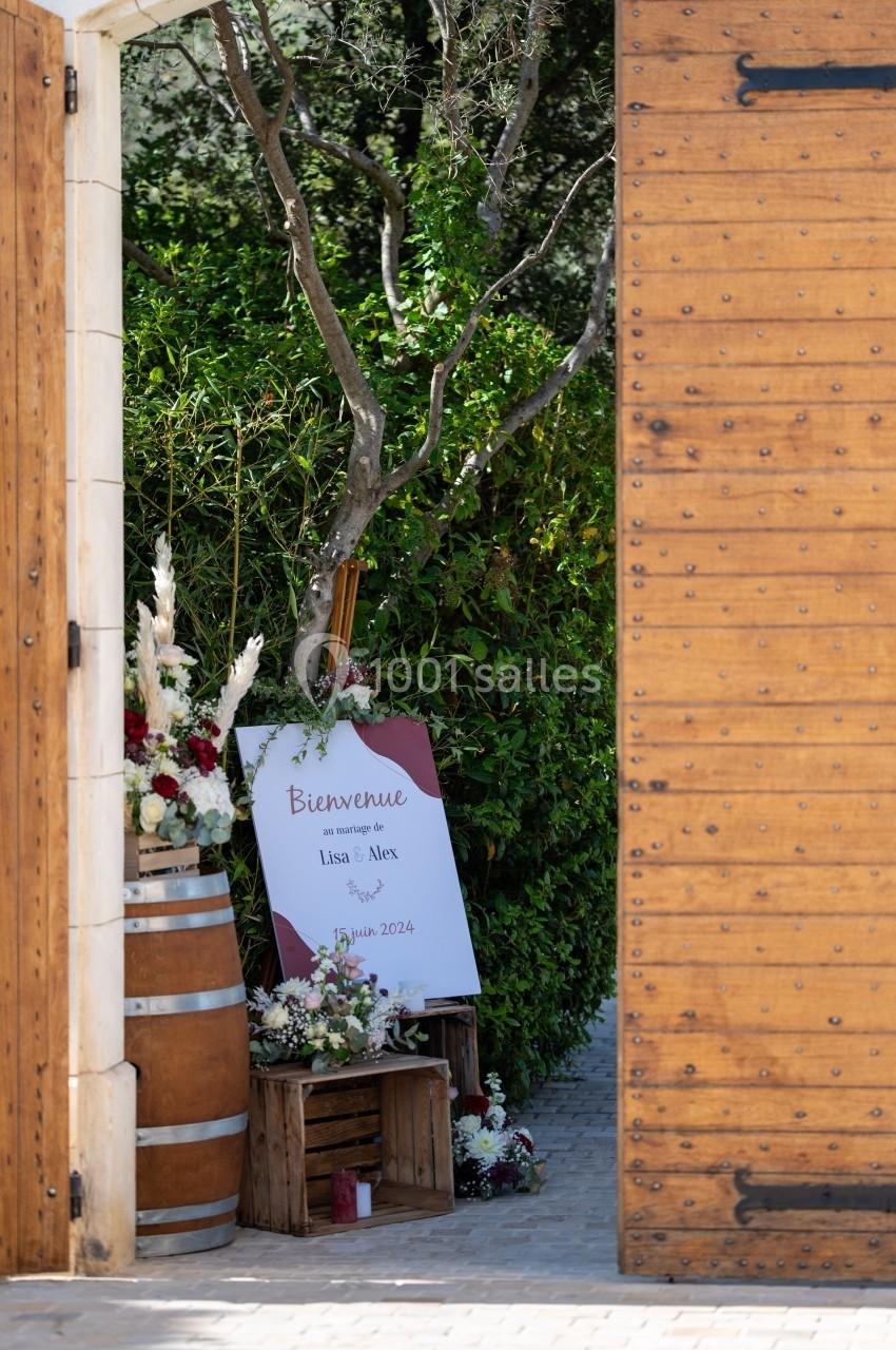 Entrée ouverte sur un jardin avec un panneau de bienvenue pour un mariage, entouré de fleurs et de décorations rustiques.