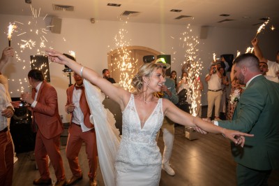 Un couple en tenue de mariage s'enlace dans un champ entouré d'oliviers sous une lumière douce.