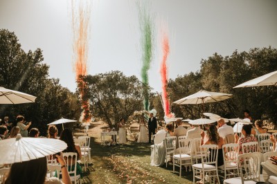 Un couple en tenue de mariage s'enlace dans un champ entouré d'oliviers sous une lumière douce.