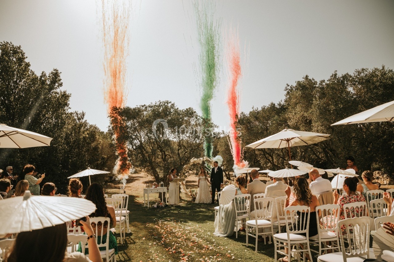 Cérémonie de mariage en extérieur avec des invités assis, des jets de fumée colorée et un couple à l'autel.