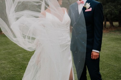 Un couple en tenue de mariage s'enlace dans un champ entouré d'oliviers sous une lumière douce.