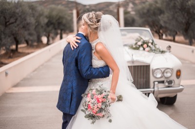 Un couple en tenue de mariage s'enlace dans un champ entouré d'oliviers sous une lumière douce.