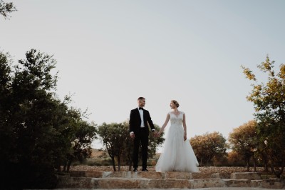 Un couple en tenue de mariage s'enlace dans un champ entouré d'oliviers sous une lumière douce.
