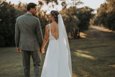 Un couple en tenue de mariage s'enlace dans un champ entouré d'oliviers sous une lumière douce.