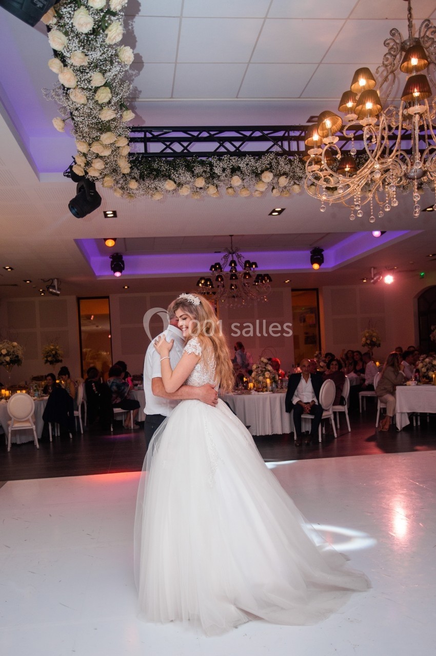Un couple danse sous des lustres et une arche fleurie dans une salle de réception décorée pour un événement festif.