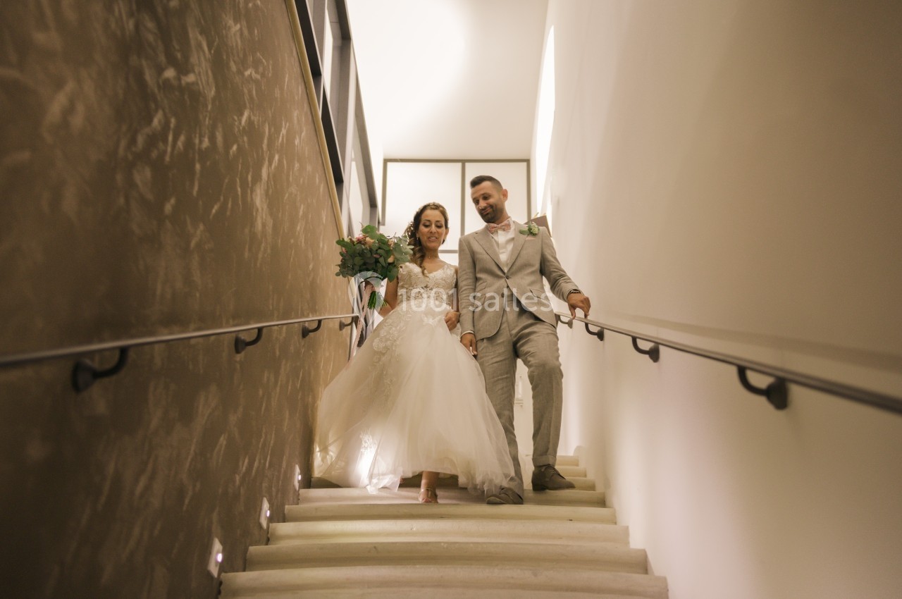 Un couple en tenue de mariage descend un escalier éclairé dans un intérieur moderne.