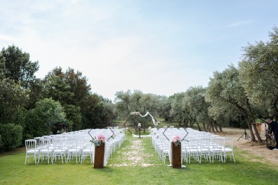 Un couple en tenue de mariage s'enlace dans un champ entouré d'oliviers sous une lumière douce.