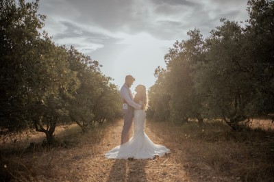 Un couple en tenue de mariage s'enlace dans un champ entouré d'oliviers sous une lumière douce.