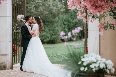 Un couple en tenue de mariage s'enlace dans un champ entouré d'oliviers sous une lumière douce.