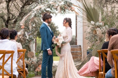 Un couple en tenue de mariage s'enlace dans un champ entouré d'oliviers sous une lumière douce.