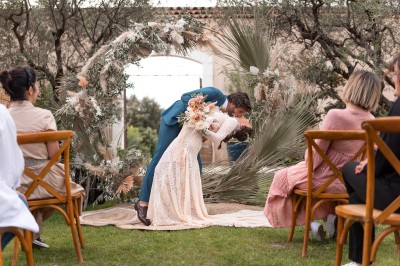 Un couple en tenue de mariage s'enlace dans un champ entouré d'oliviers sous une lumière douce.