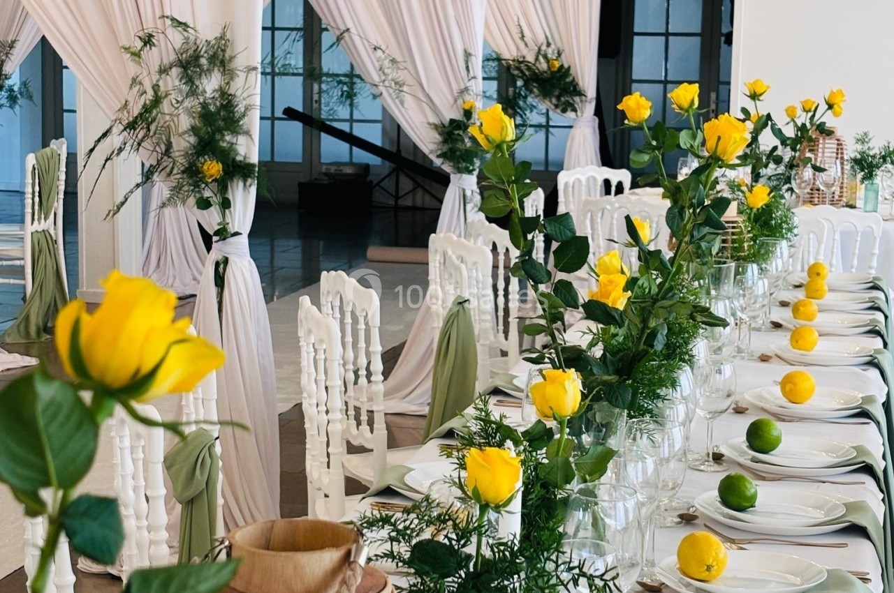 Location salle Hem (Nord) - Le Comte #6 Table décorée avec des roses jaunes, des citrons et des limes, entourée de chaises blanches et de rideaux blancs élégants.