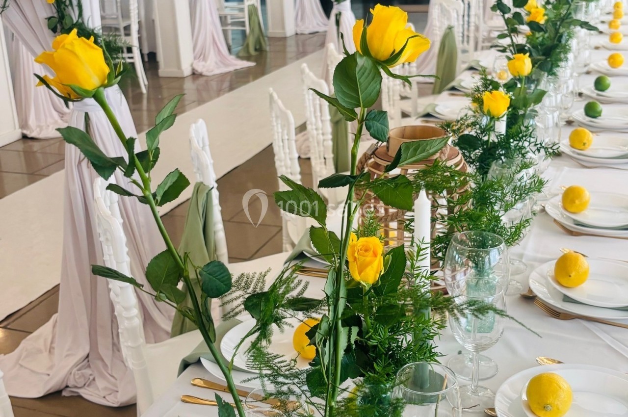 Location salle Hem (Nord) - Le Comte #10 Table décorée avec des roses jaunes, des citrons et des éléments verts dans une salle lumineuse aux rideaux blancs.