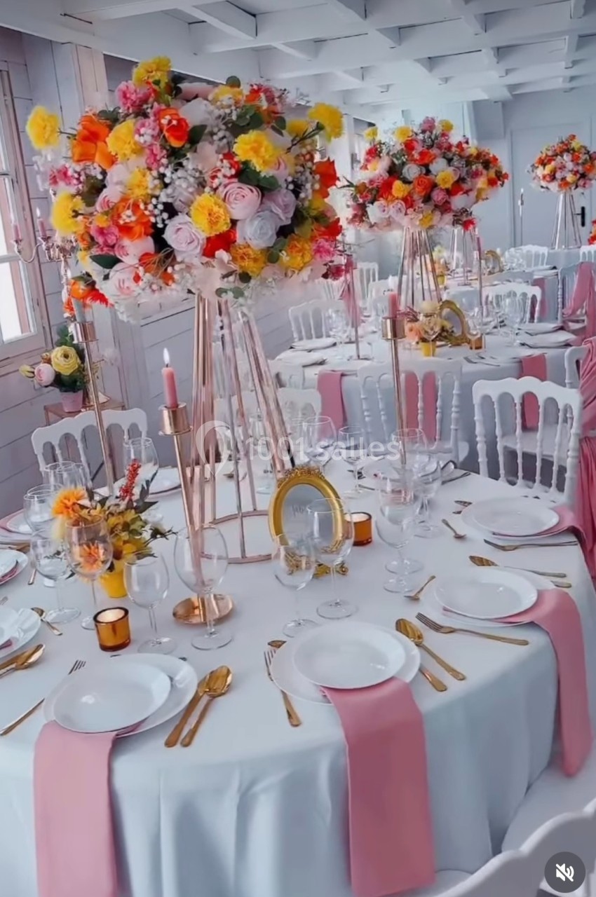 Location salle Hem (Nord) - Le Comte #17 Salle de réception décorée avec des tables rondes, nappes blanches, serviettes roses et centres de table fleuris colorés.