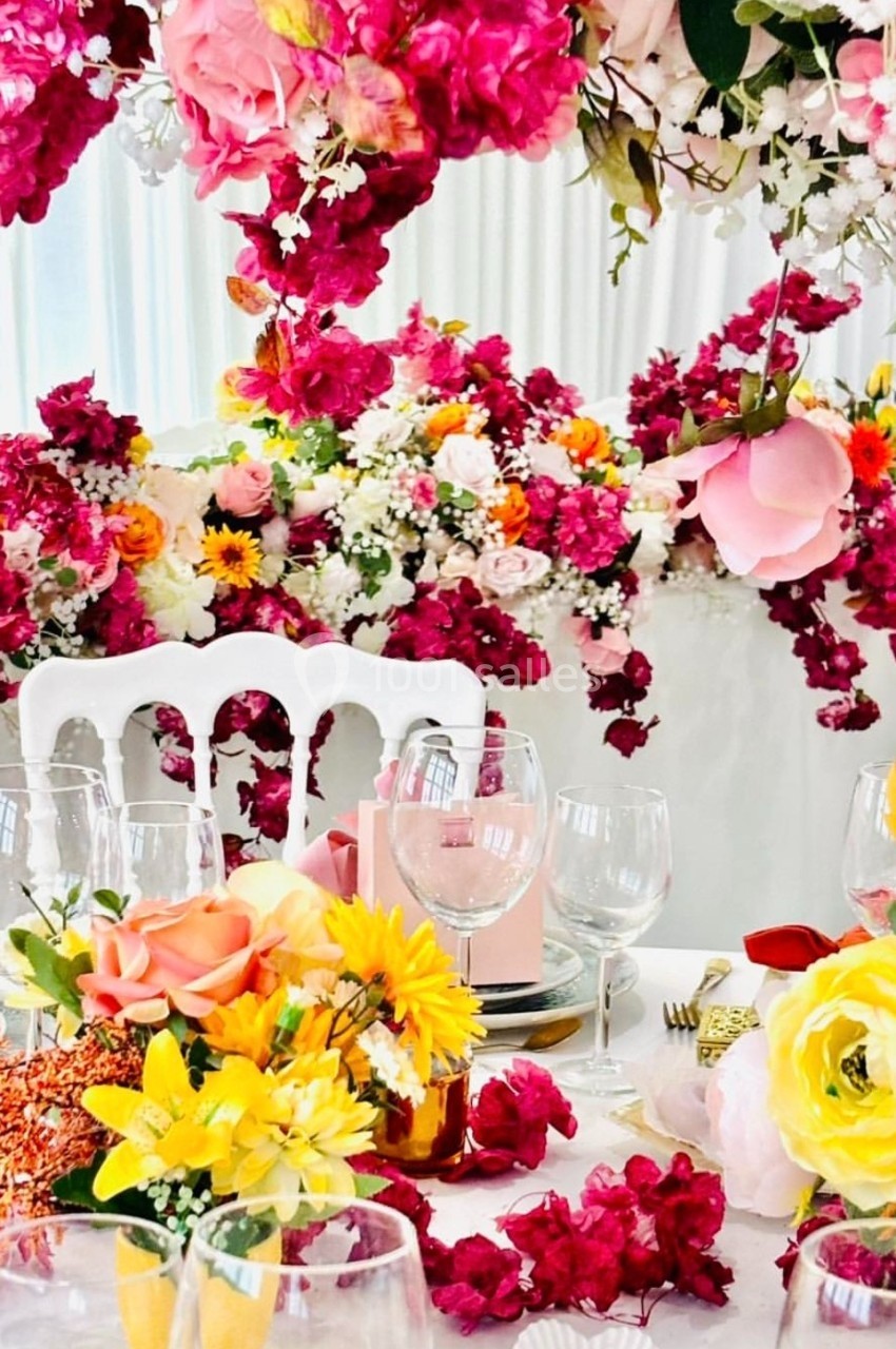 Location salle Hem (Nord) - Le Comte #16 Table décorée avec des fleurs colorées, des verres et des assiettes, entourée d'une abondance de compositions florales.