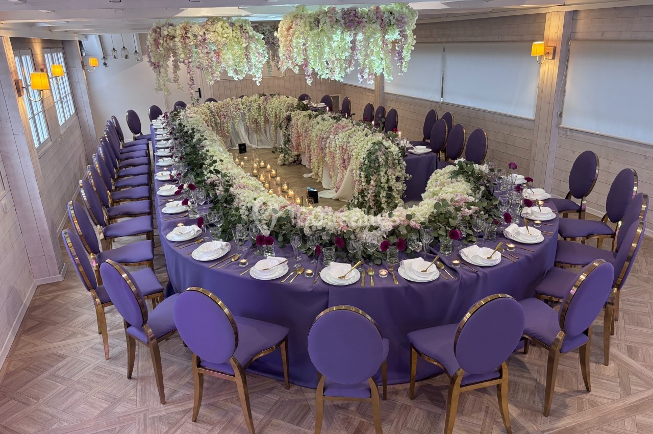 Location salle Hem (Nord) - Le Comte #26 Salle de réception avec une grande table ovale décorée de fleurs blanches et violettes, nappes violettes et chaises…