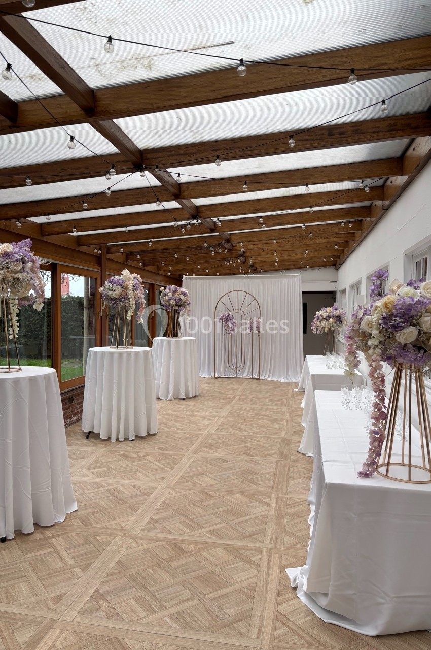 Location salle Hem (Nord) - Le Comte #28 Salle décorée pour un événement, avec tables hautes drapées de blanc et ornées de bouquets pastel sous une verrière.