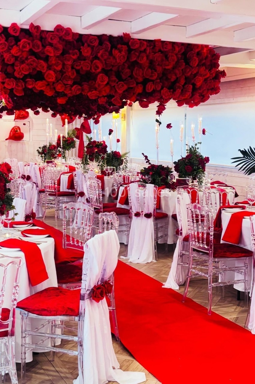 Location salle Hem (Nord) - Le Comte #13 Salle de réception décorée avec des roses rouges, nappes blanches, chaises transparentes et tapis rouge au centre.