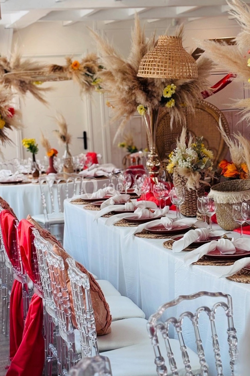 Location salle Hem (Nord) - Le Comte #19 Table décorée pour un événement, avec nappes blanches, chaises transparentes, fleurs séchées et accents rouges.