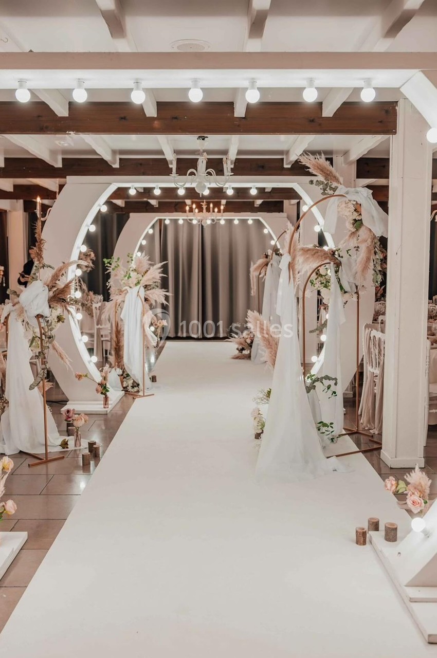 Location salle Hem (Nord) - Le Comte #1 Allée décorée pour un mariage avec arches lumineuses, voilages blancs et arrangements floraux dans une salle élégante.