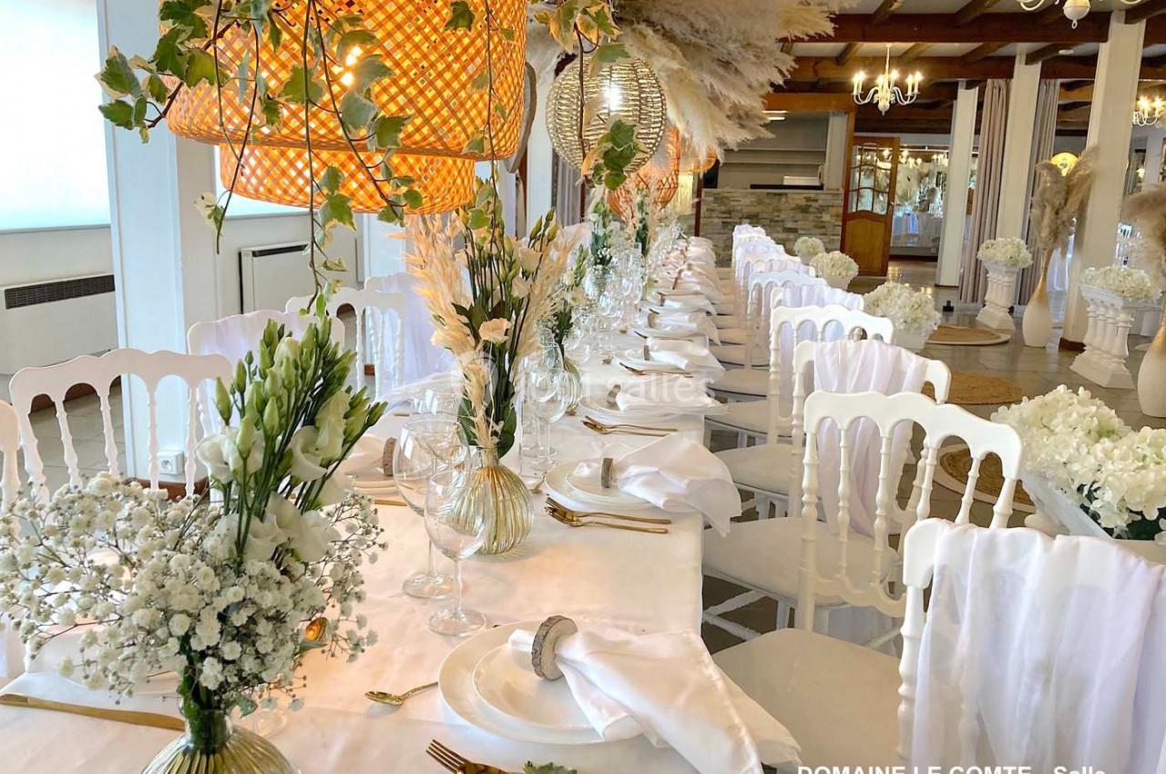 Table de réception élégamment dressée avec nappes blanches, chaises assorties et décorations florales raffinées.